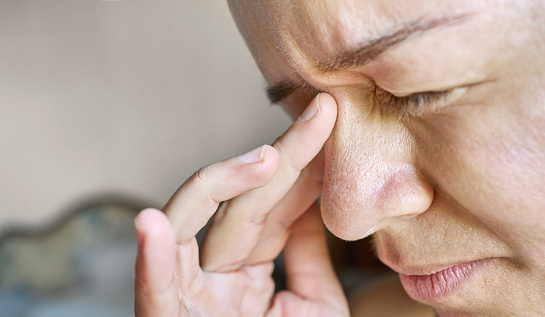 Closeup of a female touching her eye while suffering from migraine indoors