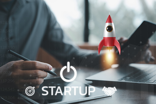 Business startup concept with a businessman controlling a white rocket icon that is taking off from a laptop into space, symbolizing the limitless potential of technology and innovation.