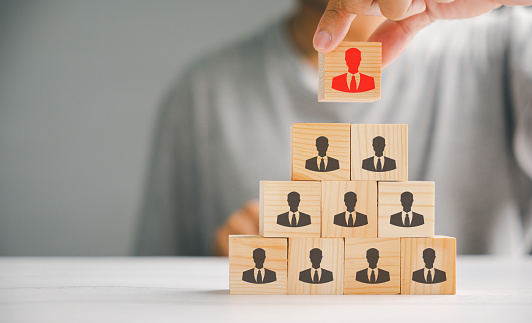 Hand holding and choosing man people icons on cube wooden toy blocks stacked. Represents the importance of human resources, teamwork, and effective leadership in achieving success.