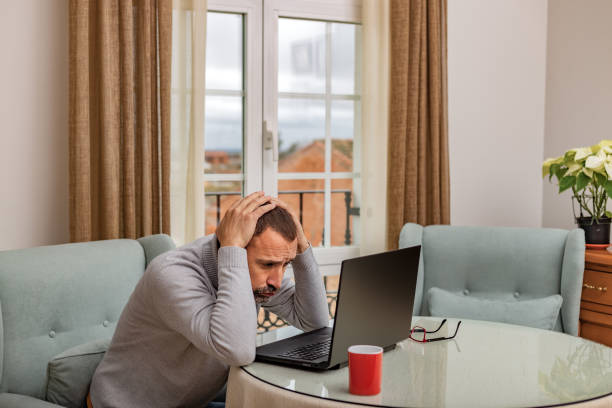 istock Adult man inside house in front laptop computer with his hands on his head and concerned expression, regretting something he has seen on the laptop screen. 1502775503