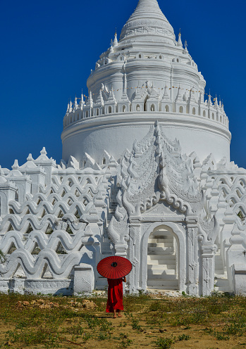 A Buddhist novice monk with a red umbrella coming to the white temple.