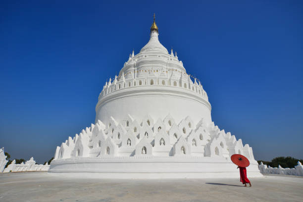 A Buddhist novice monk walking around the white stupa in sunny day.
