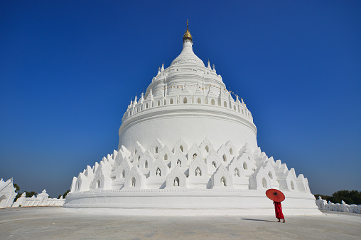 A Buddhist novice monk walking around the white stupa in sunny day.