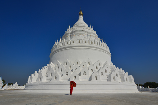 A Buddhist novice monk walking around the big stupa of white temple in sunny day.