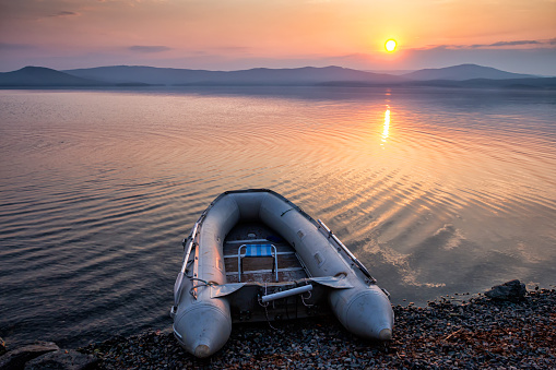 Rubber boat on the shore of the picturesque coast against the backdrop of sunrise