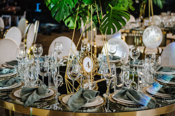 istock Round served banquet tables ready for guests, decorated table with plate, glasses, forks, emerald green napkins. Elegant dinner table. Beautifully organized event. Wedding hall with atmospheric decor. 1502787721