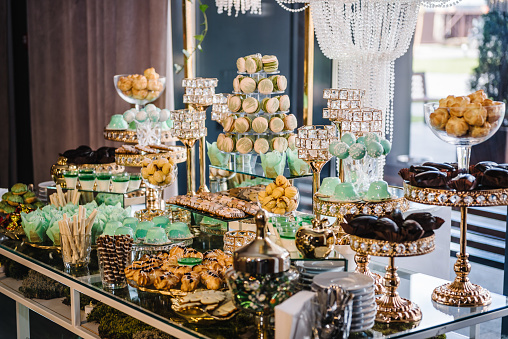 Delicious wedding reception. Birthday candy bar on the background golden luxury decor. Celebration concept. Table with sweets, candies, dessert for party. Catering. Decorating an event in restaurant.