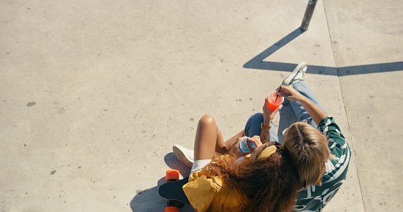 Love, skateboard and a couple drinking a beverage outdoor together in a skatepark for bonding from above. Date, summer or hobby with a young man and woman sharing a drink of juice with mockup