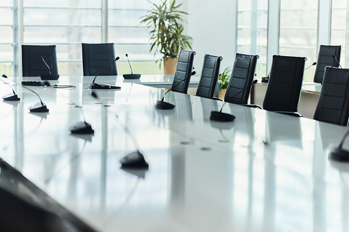 Wooden conference room interior with meeting table and armchairs, grey concrete floor. Board with laptop and tv display on wall, panoramic window on Kuala Lumpur. 3D rendering