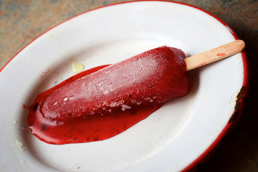 Melting strawberry lolly on a metal plate.