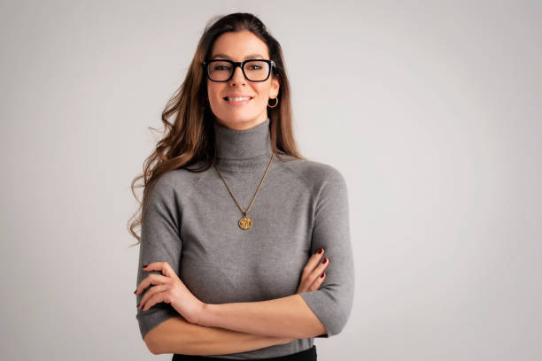 Portrait of an attractive brunette haired woman cheerful smiling against isolated background Attractive brunette haired woman standing with arms crossed at isolated background. Mid aged female wearing sweater and looking at camera. Copy space. Female wearing eyewear. high collar stock pictures, royalty-free photos & images