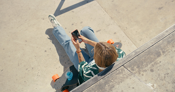 Phone, skater and text at a skate park with technology and online on social media. Digital, above view and outdoor in the sun with skateboard and mobile message relax in summer on a free web app