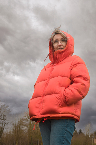 Clothing for women in bad weather. Woman in a red jacket. Portrait against a cloudy sky.