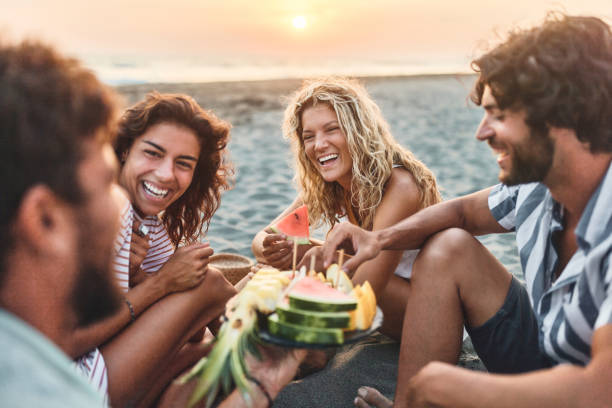 istock Happy couples talking while eating fruit on the beach at sunset. 1502801510