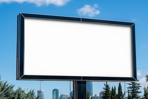 Blank white advertising billboard. City silhouette in the background. Summer time