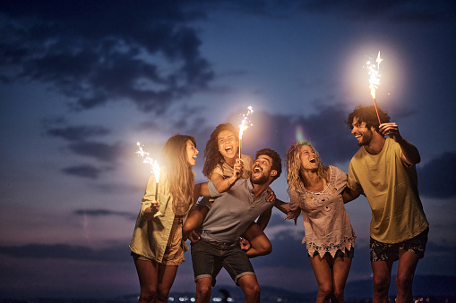 Young cheerful friends having fun with flaming torches during the night on the beach. Copy space.