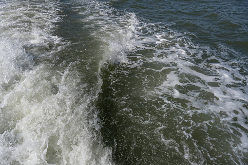 A ship discharging ballast into the ocean. Only part of the ship is visible. Part of a pier behind ship. Hull is red and white.