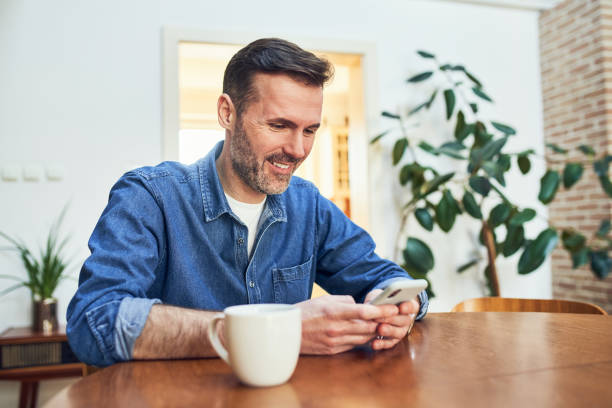 istock Smiling adult man at home sitting at table using smart phone 1502802225