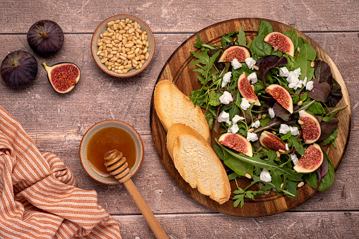 Food photography of salad with goat cheese, figs, leaves, pine nuts, toast, honey