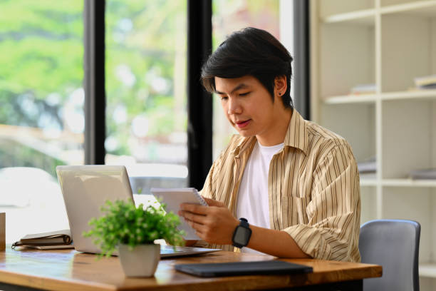 istock Millennial asian businessman sitting at office desk checking schedule or handwriting important information. 1502834116