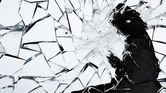 Silhouette of a girl looking at her phone distorted by broken glass.