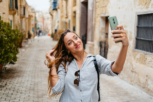 Beautiful young woman taking selfies using her smart phone on the street in Valletta, Malta.