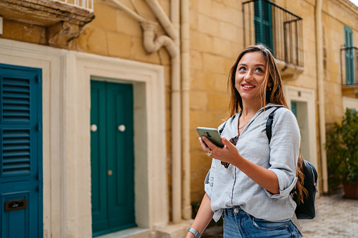 Beautiful young female tourist looking up directions on a smart phone in Valletta, Malta.