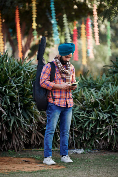 молодой индийский сикх в бирюзовом головном уборе пагри, красной рубашке и синих джинсах с гитарой - new delhi audio стоковые фото и изображения