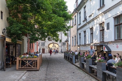 Riga, Latvia – June 15, 2023: Tourists in a street cafe in the Old Town of Riga, the Swedish Gate in the background