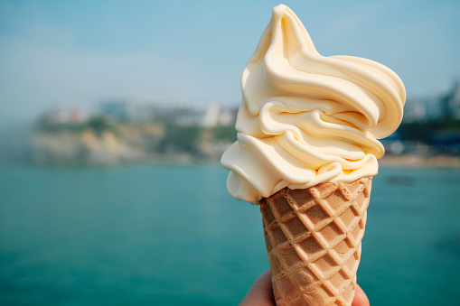 Hand holding an Ice Cream with Newquay town defocused in the background.