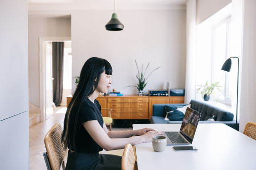 With her laptop and a cup of coffee by her side, a woman confidently thrives in her home office. This image captures her appreciation for the freedom that comes with being a successful female entrepreneur.