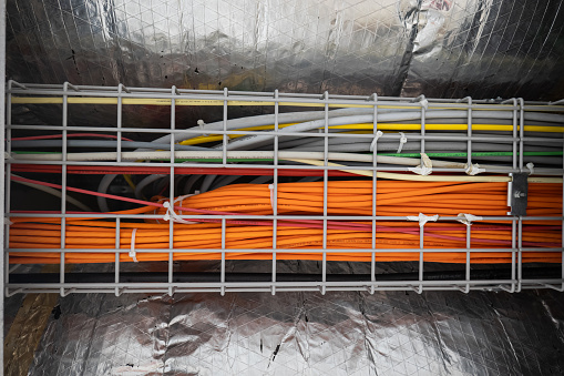 Bundle of orange ethernet cables routed in a building ceiling along the ventilation system. Bottom-angle view, no people