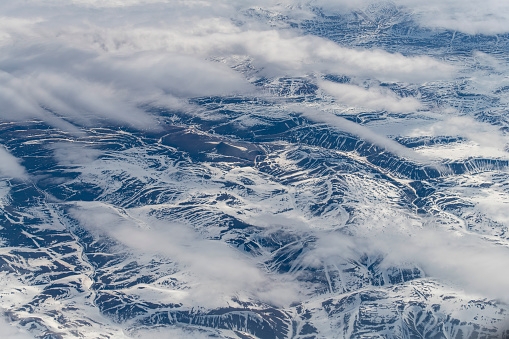 Aerial view at 38,000 feet of part of the mountains and hills on landmass of Nunavut, a territory of northern Canada, forming most of the Canadian Arctic Archipelago partly covered in snow