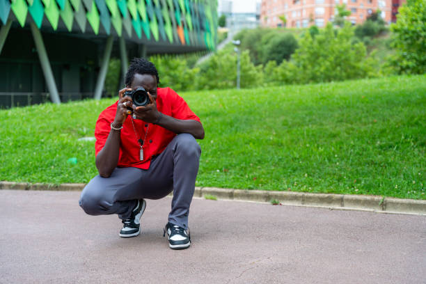 istock Young black photographer taking pictures with a digital camera. with the camera looking through the lens in a park in Bilbao, in front of the Bilbao Arena, sports palace of Bilbao. Young black profess 1502872694