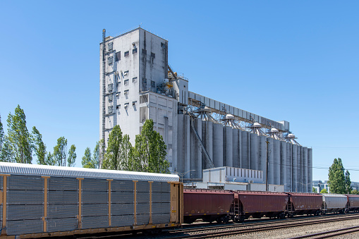 Seatlle, WA, USA-July 2022; View of a large grain elevator complex near port facilities for export with train tracks and train hopper cars and autorack cars in forefront
