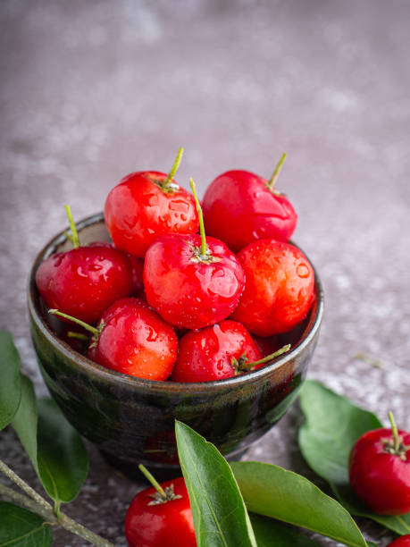 istock Ripe red cherries in a ceramic bowl with leaves on stone background. 1502875185