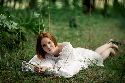 A woman lies on a green glade on a pillow in the forest. Rest, relaxation in nature, recovery of vitality.