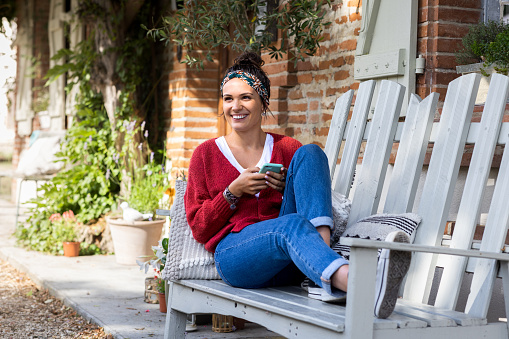 A young woman who is on holiday in Toulouse in the south of France. She is sitting outdoors and checking her social media on a smartphone with a smile.