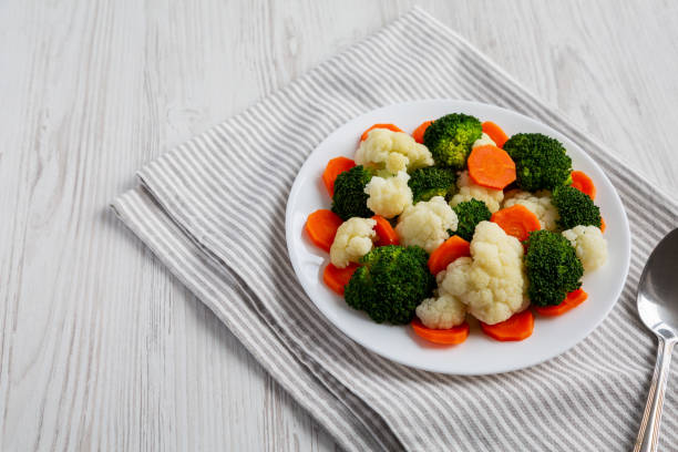 istock Mixed Organic Steamed Vegetables (Carrots, Broccoli and Cauliflower) on a Plate on a white wooden background, low angle view. Copy space. 1502878040