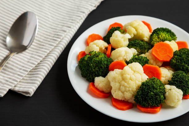 istock Mixed Organic Steamed Vegetables (Carrots, Broccoli and Cauliflower) on a Plate on a black surface, side view. 1502878071