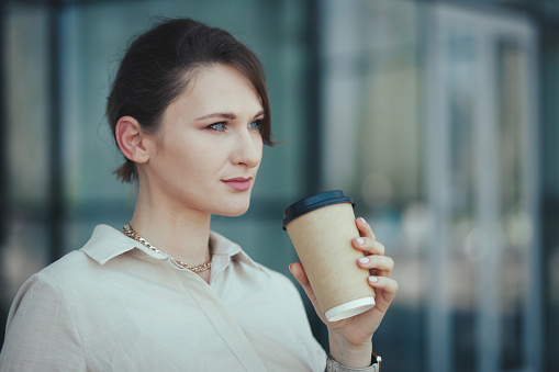 Portrait of young business woman holding in hands paper cup with takeaway coffee or other beverage.