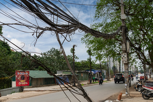 Hanoi, Vietnam-April 2023; View along one of the streets of the city, lined with electricity cables, telephone lines hanging in disarray and chaotically ordered on a concrete pole