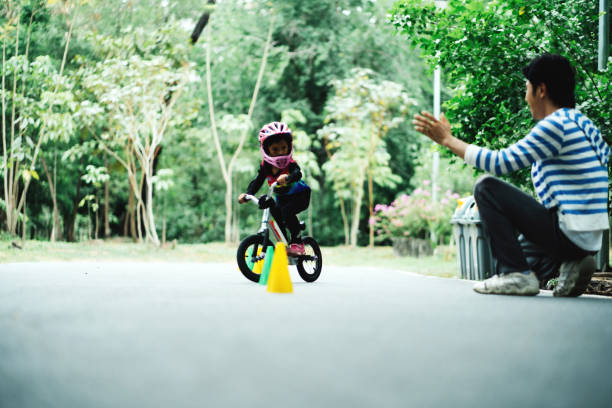 Father running by child learning cycling on footpath at park, teaching kid to ride bicycle on road