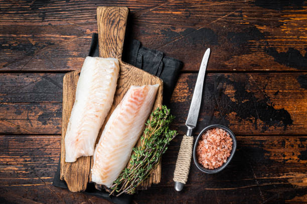 istock Cod fish fillets, raw codfish with thyme on wooden board. Wooden background. Top view 1502880661