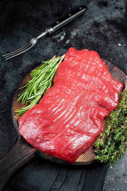 istock Raw flank beef steak, uncooked meat with herbs. Black background. Top view 1502881224
