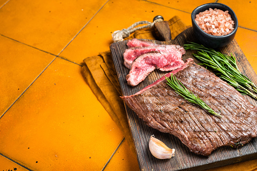 BBQ dry aged wagyu Flank Steak on a cutting board. Orange background. Top view. Copy space.