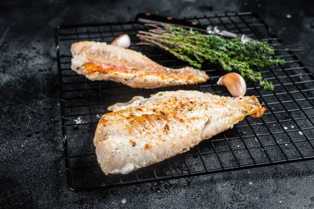 Photo of Grilled sea red perch fillet, Snapper fish on a rack. Black background. Top view