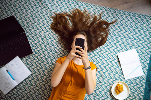 Adolescente caucásica pelirroja, tirada en el suelo y usando el teléfono móvil photo