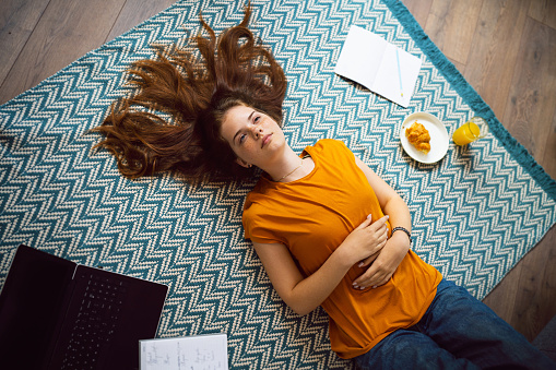 Pensive redhead Caucasian teenage girl, lying on the floor, while taking a break from studying