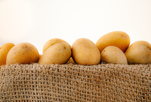 fresh, raw, young potatoes in a sack, jute sack. Detail shot with selective sharpness on the coarse fabric and front potatoes
